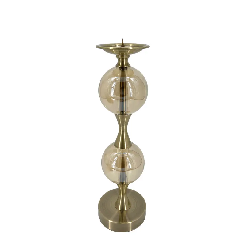 Κηροπήγιο ύψους 42 cm και διαμέτρου 12 cm, κατασκευασμένο από ανθεκτικό μέταλλο σε κομψή μπρονζέ απόχρωση. Διαθέτει δύο διακοσμητικές γυάλινες μπάλες σε διάφανη απόχρωση, που προσθέτουν φινέτσα και ελαφρότητα στον σχεδιασμό. Κατάλληλο για κλασικά κεριά (όχι ρεσώ), αποτελεί ιδανική επιλογή για τραπέζι, μπουφέ ή κεντρικό διακοσμητικό σε ειδικές περιστάσεις.